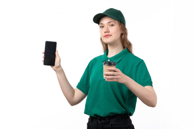 Un giovane corriere femminile di vista frontale in uniforme verde che tiene lo smartphone della tazza di caffè e che sorride sul bianco