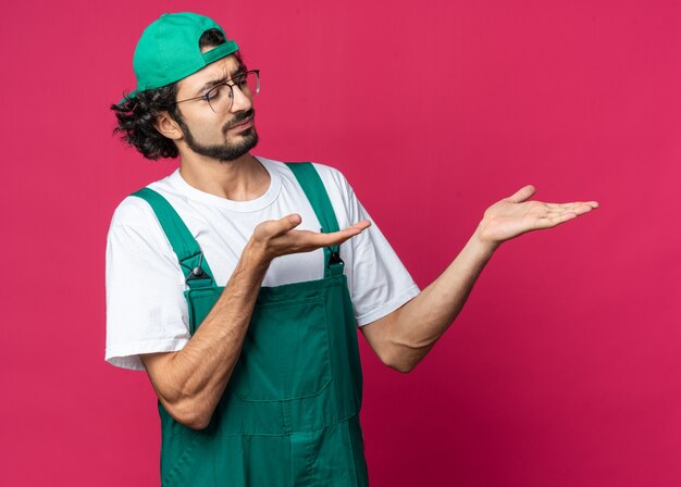 Un giovane costruttore scontento che indossa l'uniforme con il berretto che finge di tenere qualcosa