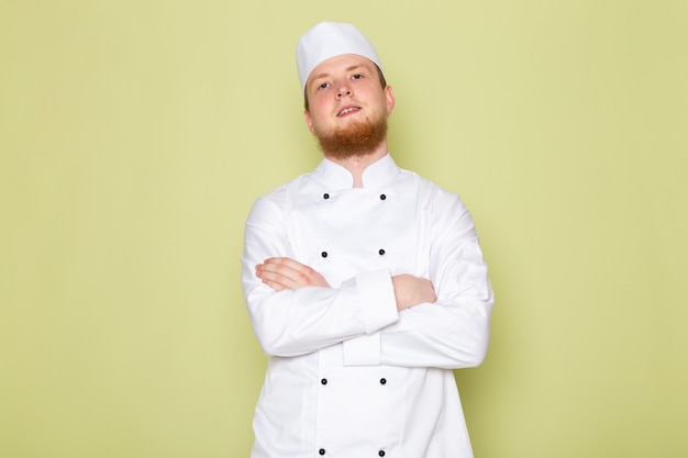 Un giovane cuoco maschio di vista frontale in cappuccio bianco del vestito bianco del vestito da cuoco che posa sorridere