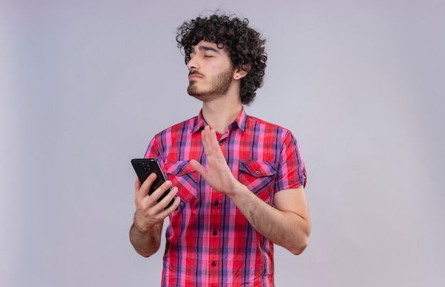 Un giovane di bell'aspetto con i capelli ricci in camicia a quadri chiudendo gli occhi tenendo il cellulare