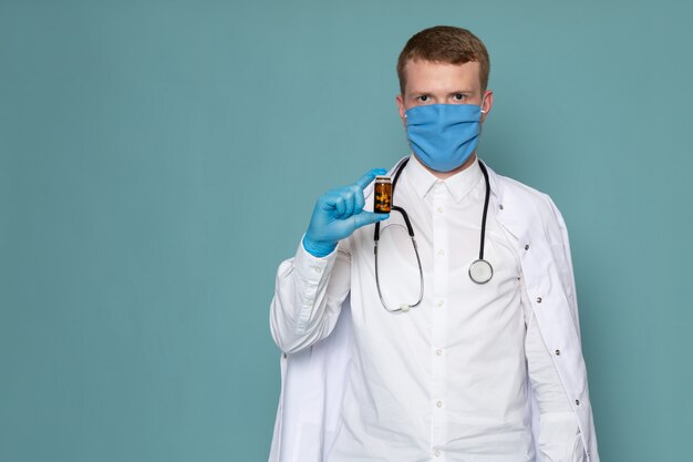 Un giovane di vista frontale in camicia bianca e guanti blu che tengono le pillole sullo spazio blu