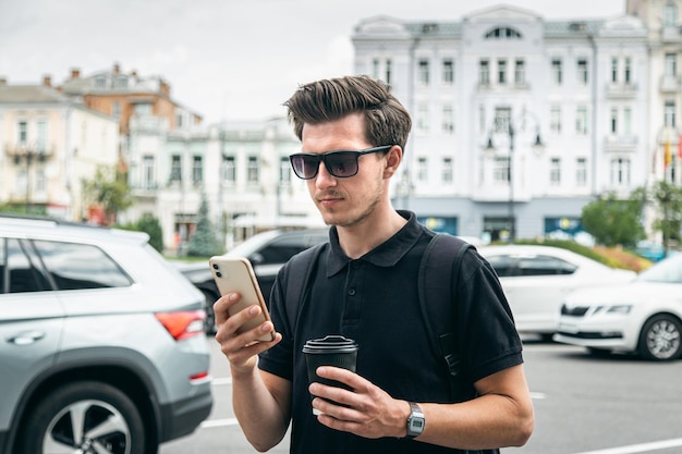 Un giovane in occhiali da sole con smartphone e caffè in città