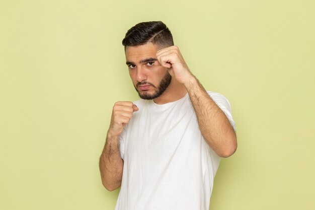 Un giovane maschio di vista frontale in maglietta bianca che posa con il supporto di boxe