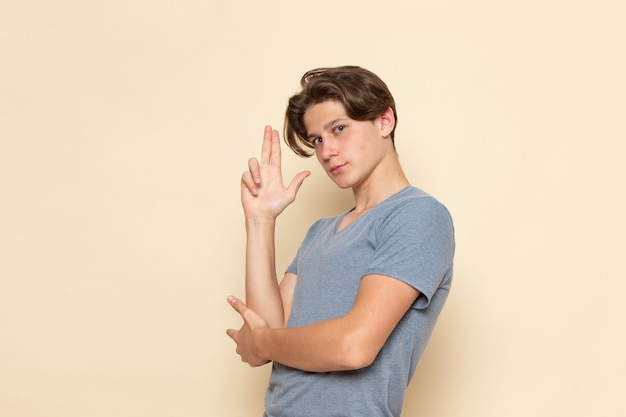 Un giovane maschio di vista frontale in maglietta grigia che posa con le mani alzate