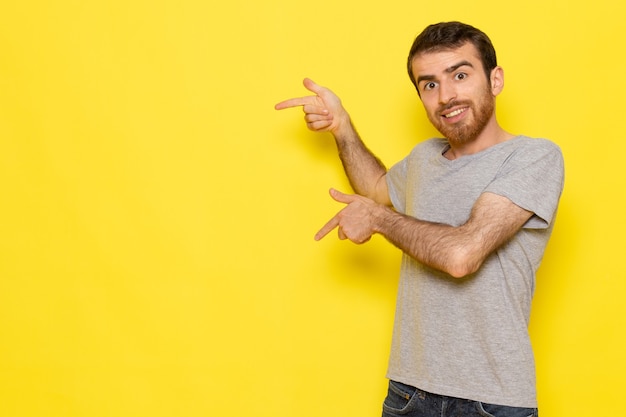 Un giovane maschio di vista frontale in maglietta grigia che sorride e che posa sui vestiti gialli di emozione del modello di colore dell'uomo della parete