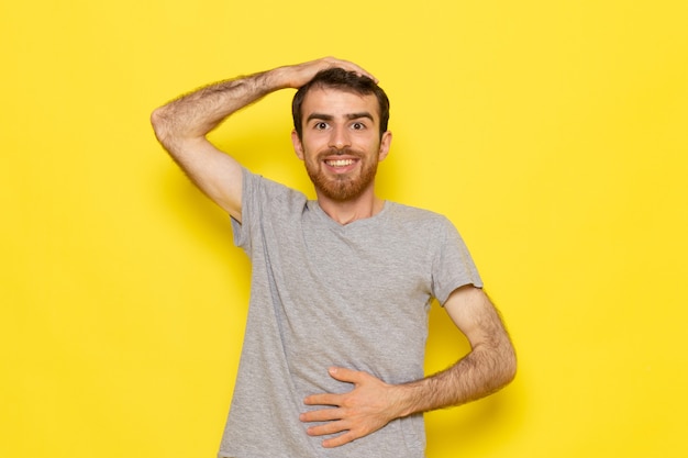 Un giovane maschio di vista frontale in maglietta grigia che sorride e che posa sui vestiti gialli di emozione del modello di colore dell'uomo della parete