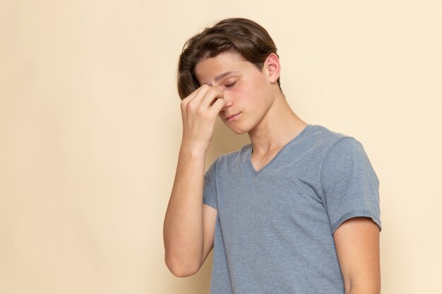 Un giovane maschio di vista frontale in maglietta grigia che tiene il suo naso