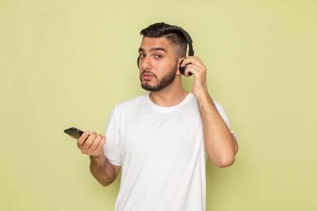 Un giovane maschio di vista frontale in t-shirt bianca che tiene telefono e ascolto di musica