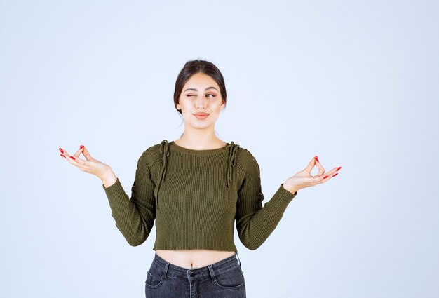 Un giovane modello in camicetta verde che fa meditazione sul muro bianco