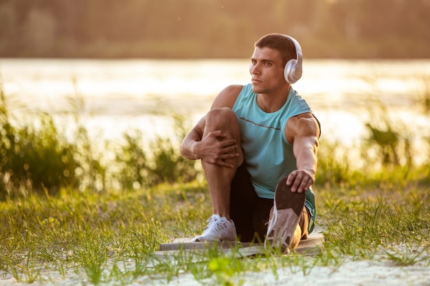 Un giovane uomo atletico che si allena ascoltando la musica in riva al fiume all'aperto