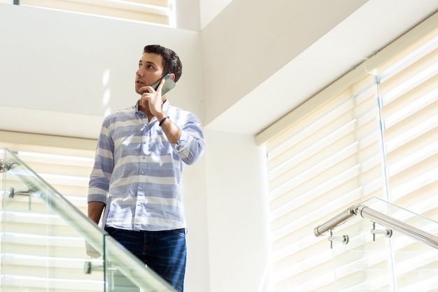 Un giovane uomo bello di vista frontale in camicia a strisce che parla e che discute le questioni di lavoro sul telefono durante la costruzione di attività di lavoro di giorno