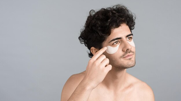 Un giovane uomo caucasico con barba ispida che si mette delle toppe sotto gli occhi