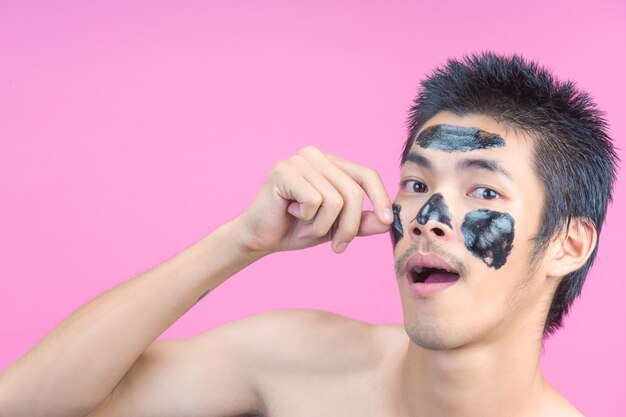 Un giovane uomo con le mani per rimuovere cosmetici neri sul viso su una rosa.