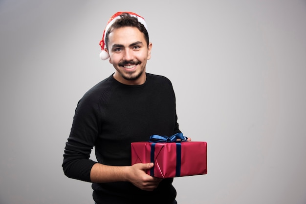 Un giovane uomo in possesso di una confezione regalo su un muro grigio.
