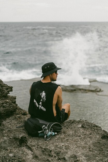 Un giovane viaggiatore con uno zaino sull'oceano sulle rocce guarda in lontananza.