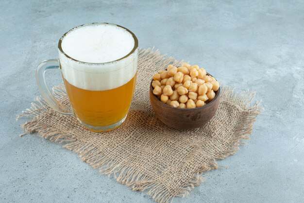 Un grande bicchiere di birra con una piccola ciotola di legno piena di piselli su tela di sacco. Foto di alta qualità