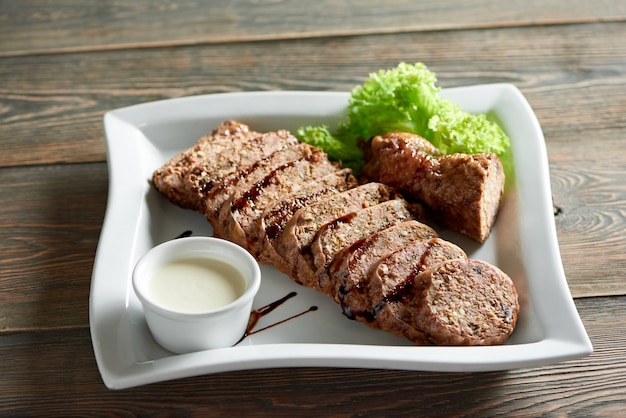 Un grande piatto bianco, servito con deliziose fette di carne ripiene con salsa all'aglio e decorato con foglie di insalata. Buon antipasto per la cena al ristorante con vino rosso.