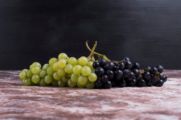 Un grappolo d'uva verde e rossa sul tavolo sul muro nero