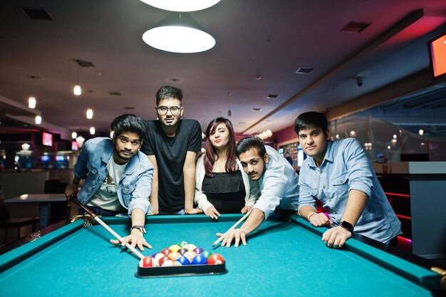 Un gruppo di amici asiatici alla moda indossano jeans che giocano a biliardo al bar.