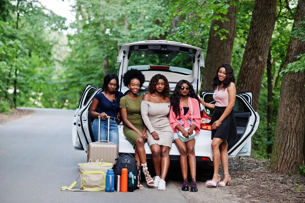 Un gruppo di cinque ragazze felici del viaggiatore afroamericano che si siedono nel bagagliaio aperto dell'auto