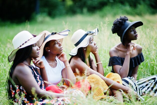 Un gruppo di quattro bellissime donne afroamericane indossano un cappello estivo seduti all'erba verde nel parco