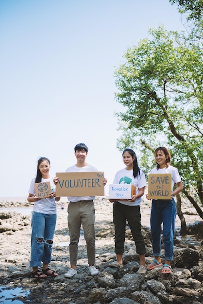 Un gruppo di volontari tiene un segno di volontariato nell'evento della giornata mondiale dell'ambiente la conservazione dei volontari raccoglie i rifiuti di plastica e schiuma sull'area della foresta di mangrovieIl volontariato salva il concetto di mondo