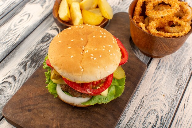 Un hamburger di pollo vista frontale con formaggio e patate insalata verde sullo scrittorio di legno e superficie grigia