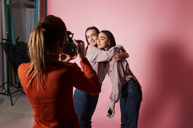 Un'immagine di due ragazze che abbracciano ciascuna e che sono fotografate da un cameraman femminile in studio