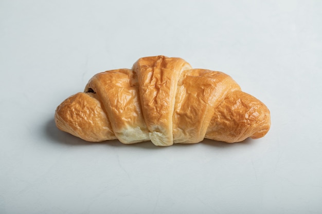 Un intero croissant delizioso fresco su sfondo bianco.