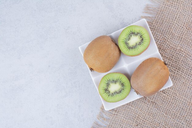 Un kiwi a fette nel piatto bianco su tela di sacco. Foto di alta qualità