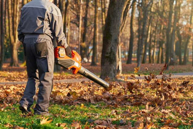 Un lavoratore maschio irriconoscibile che usa un soffiatore di foglie nel parco della città in vista posteriore di un uomo forte che indossa