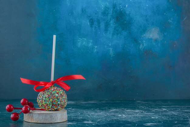 Un lecca-lecca ricoperto di caramelle e un ornamento di bacche di Natale su un pezzo di legno su sfondo blu. Foto di alta qualità