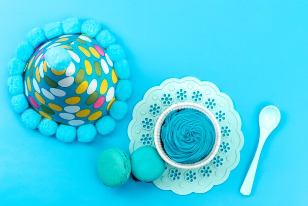 Un macarons francese blu con vista dall'alto insieme a un cucchiaio di plastica bianca da dessert blu e un tappo di compleanno sulla scrivania blu, festa di compleanno