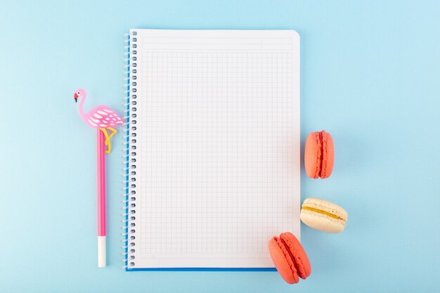 Un macarons francesi di vista superiore con la penna ed il quaderno sulla torta dolce del biscotto dello zucchero da tavola blu