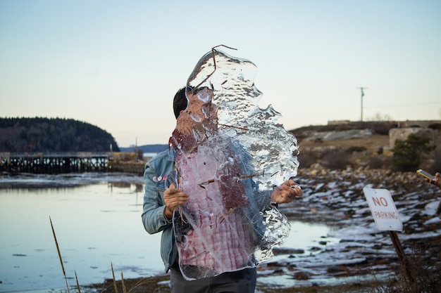 Un maschio caucasico in possesso di un gigantesco pezzo di ghiaccio nelle sue mani con un lago in background