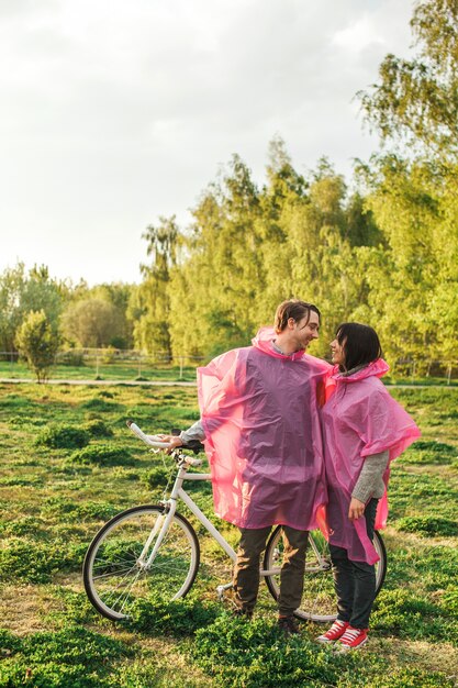 Un maschio e una femmina che si guardano romanticamente in impermeabili di plastica rosa a un appuntamento con una bicicletta
