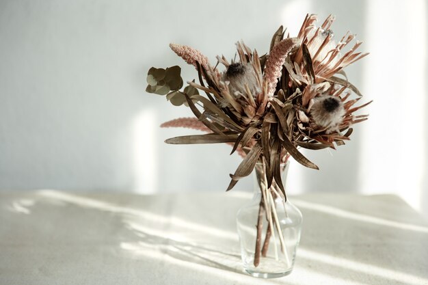 Un mazzo di fiori secchi in un vaso di vetro su uno sfondo chiaro con luce solare.