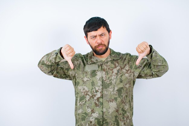 Un militare arrabbiato sta guardando la fotocamera mostrando un gesto di antipatia su sfondo bianco