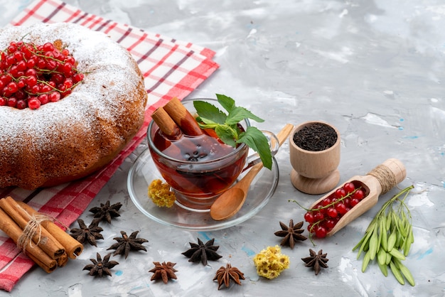 Un mirtillo rosso fresco di vista frontale acida e pastosa con tè rotondo della torta e cannella sul colore fresco dello scrittorio bianco