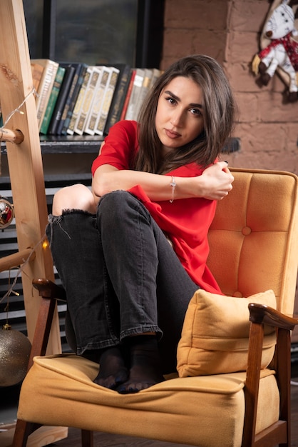 Un modello di giovane donna in camicia rossa seduta e in posa.