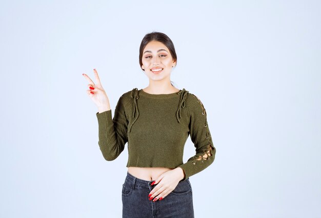 Un modello sorridente della giovane donna che sta e che mostra il segno di vittoria.