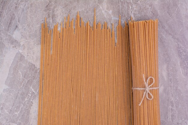 Un mucchio di spaghetti crudi su uno spazio grigio.