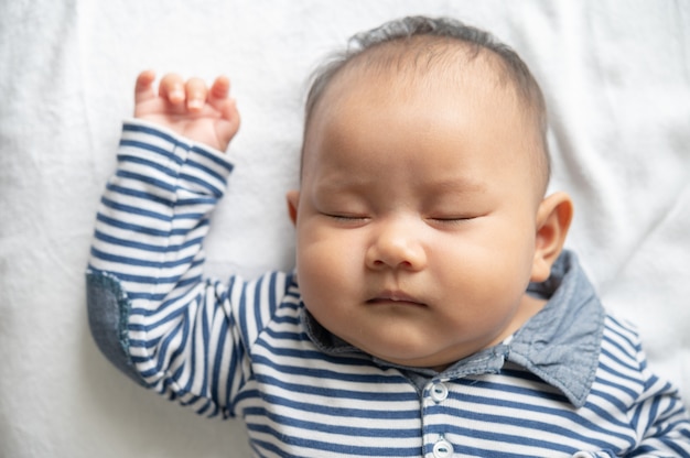 Un neonato con una camicia a righe sta dormendo nel letto.