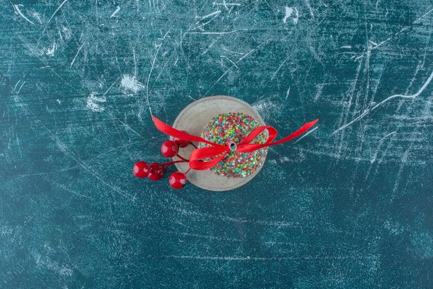 Un ornamento di bacche di Natale e un lecca-lecca su un pezzo di legno su sfondo blu. Foto di alta qualità