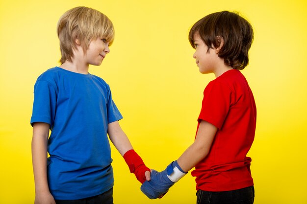 Un paio di ragazzi di vista frontale che sorridono l'un l'altro stringendosi la mano in maglietta colorata e legando le mani sulla parete gialla