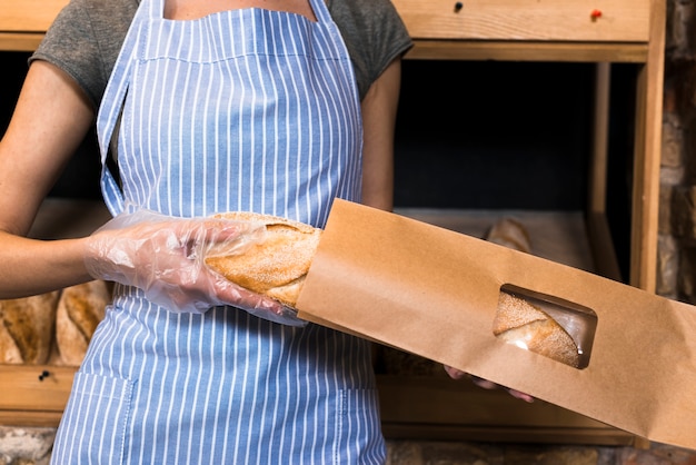 Un panettiere femmina in grembiule che impacchetta il pane baguette nel sacchetto di carta marrone