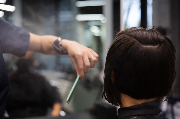 Un parrucchiere ragazza professionista fa un taglio di capelli del cliente. La ragazza è seduta in una maschera nel salone di bellezza