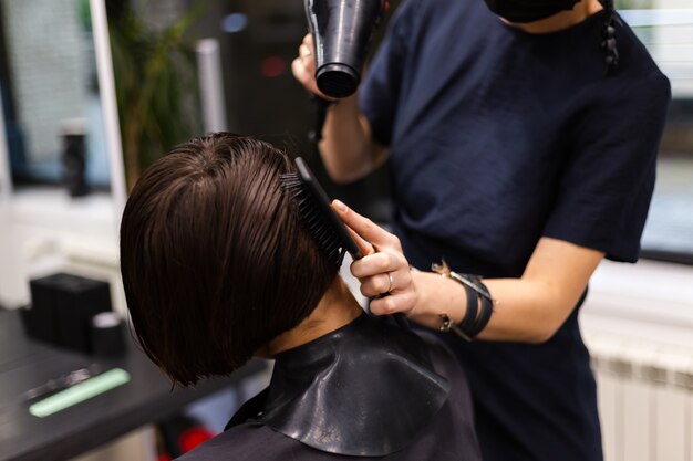 Un parrucchiere ragazza professionista fa un taglio di capelli del cliente. La ragazza è seduta in una maschera nel salone di bellezza