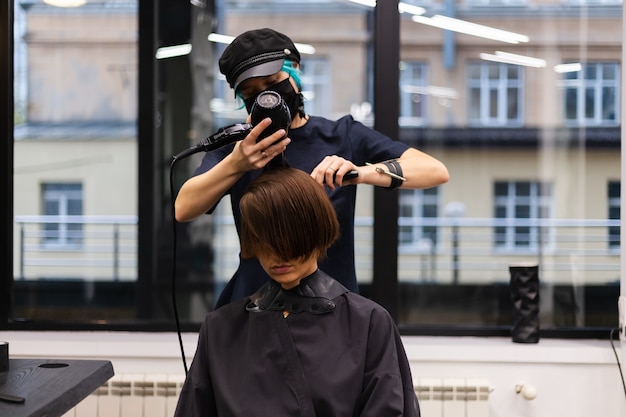 Un parrucchiere ragazza professionista fa un taglio di capelli del cliente. La ragazza è seduta in una maschera nel salone di bellezza