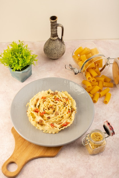 Un pasto gustoso di pasta italiana vista dall'alto con verdure cotte e fettine di carne all'interno della lastra grigia insieme a fiori e pasta cruda sul rosa